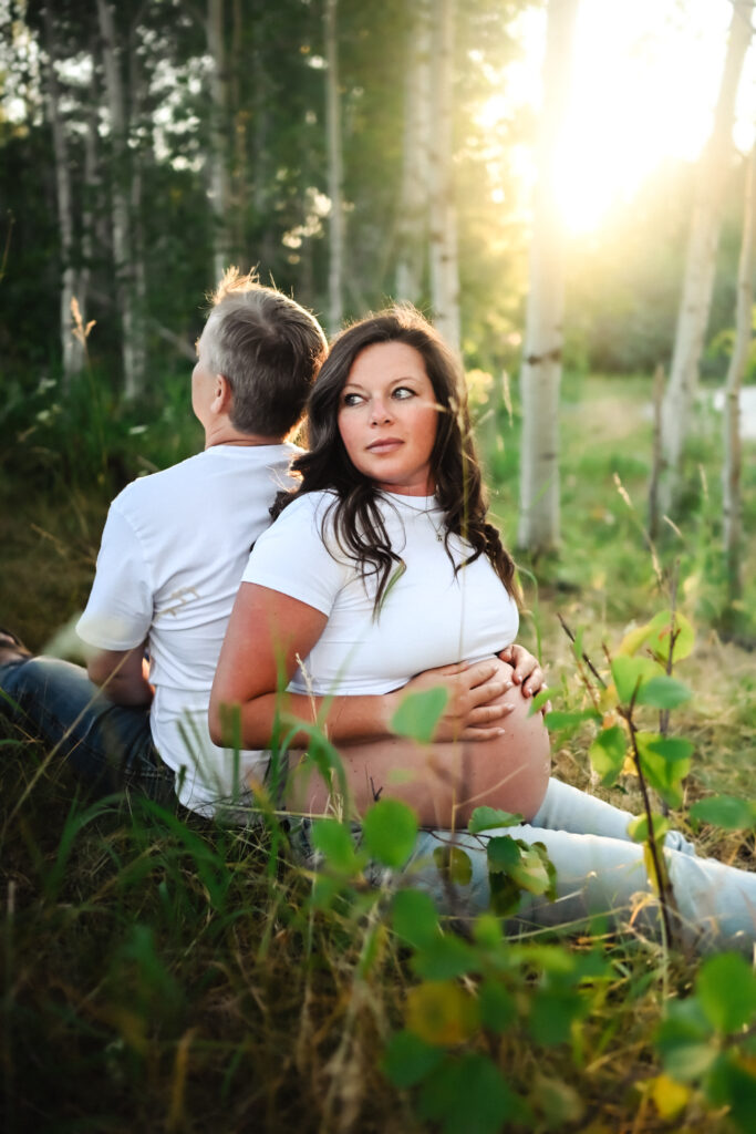 Pregnant mama sitting in field with sunshine and husband during her driggs maternity session