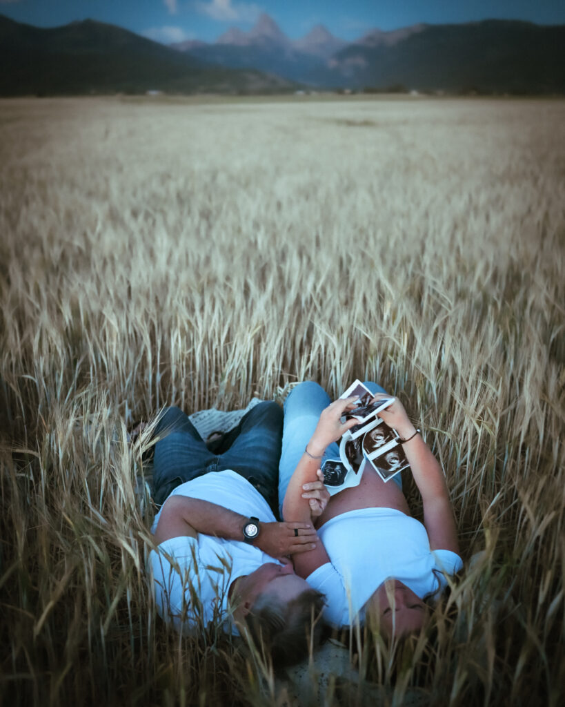 Pregnant mama holding her ultrasound while laying down in a field near near the Tetons during her Driggs Maternity session