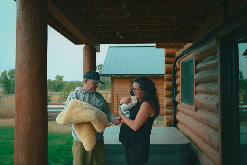 New mom and dad outside with baby and sheepskin blanket during newborn photography session