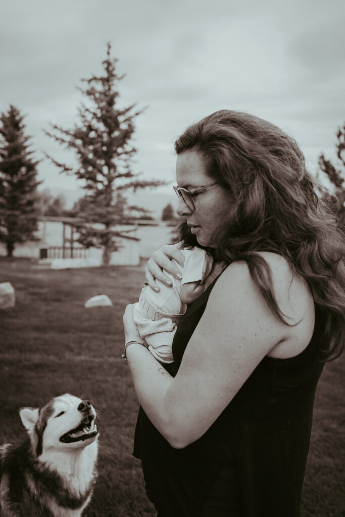 Dog looking at new mom holding newborn baby outside at newborn photography session