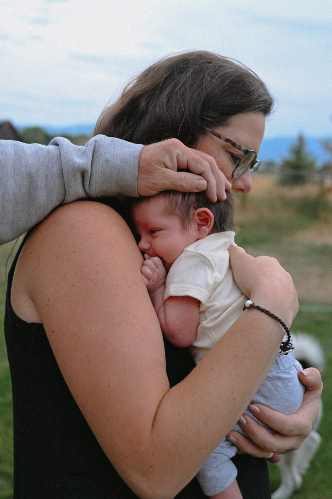 Mom holding newborn baby with dads hand placed gently on newborns head captured by newborn photographer Sara O'Connell