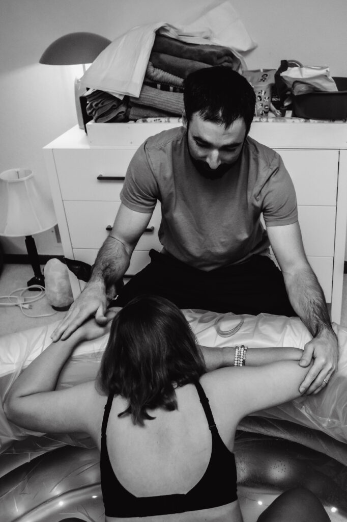 Woman laboring with husband nearby to support her captured by birth photographer at home birth