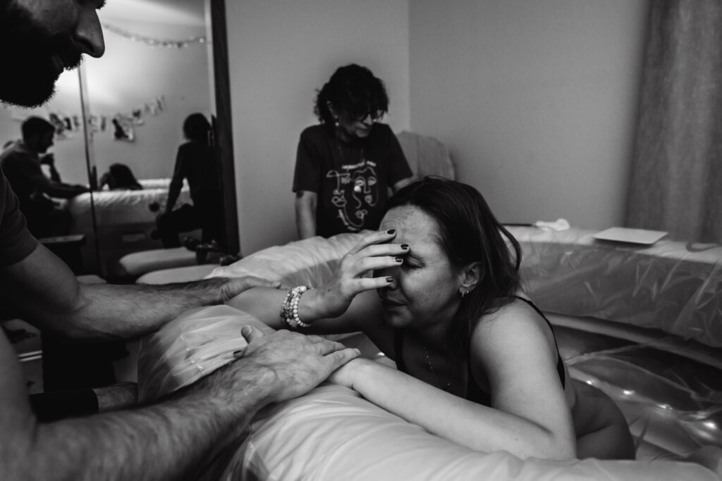Tired mother laboring in birth pool at home birth captured by birth photographer