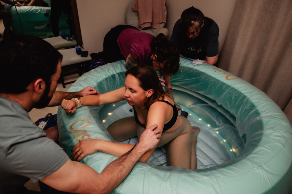 Mother giving birth in birth pool during home birth captured by birth photographer