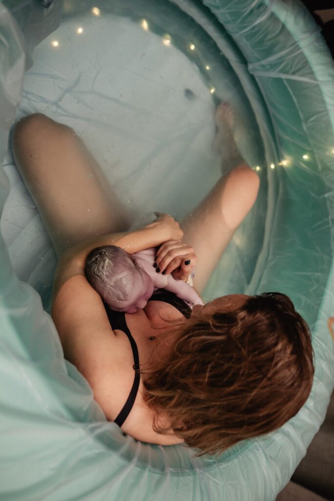 Newborn baby in mothers arms after just being born in birth pool