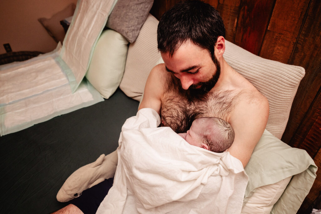 Dad cuddled up skin to skin with newborn baby in bed