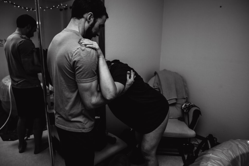 Laboring mother leaning on husband during birth captured by birth photographer